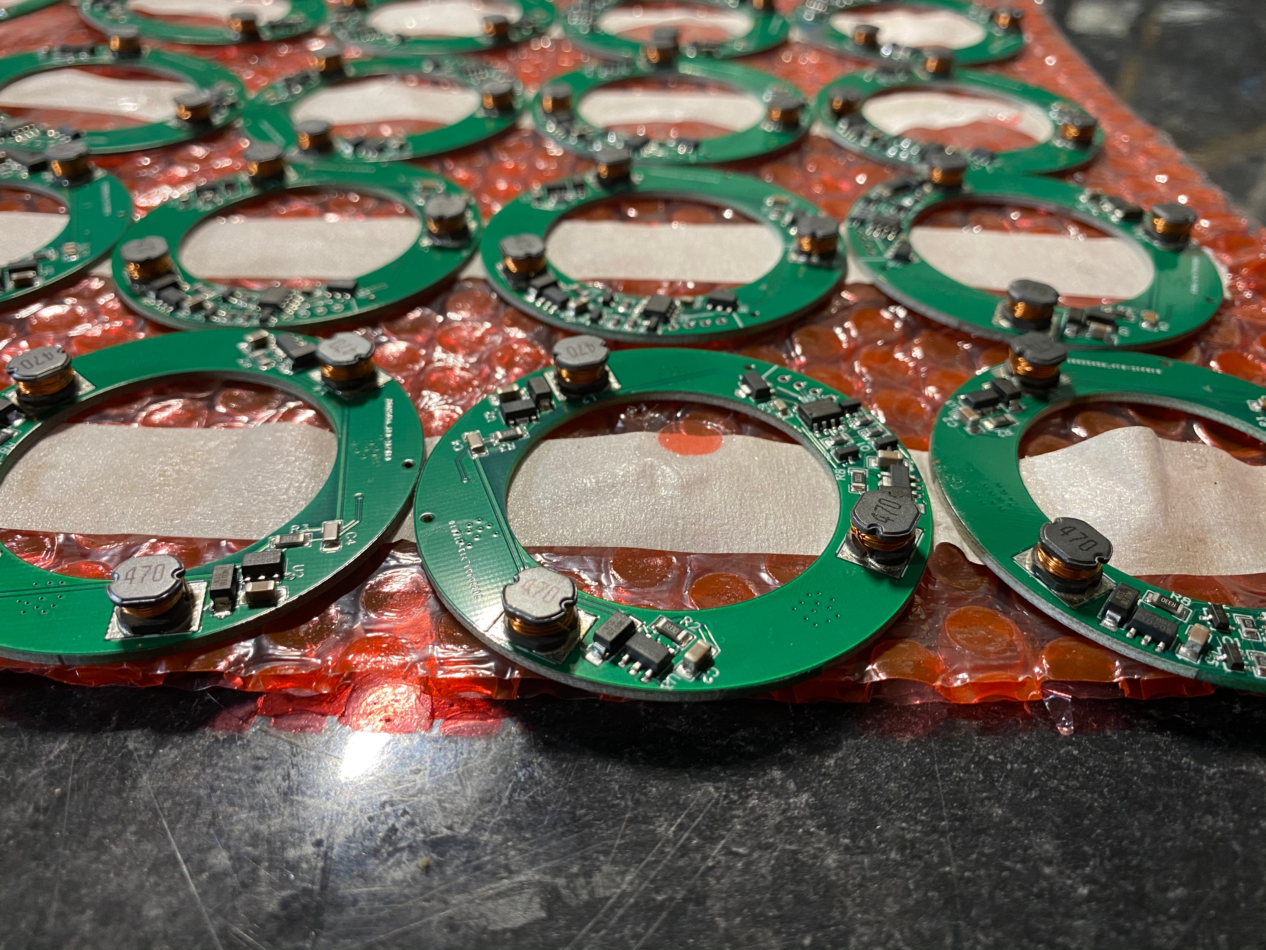 Close-up of multiple custom designed circular green printed circuit boards (PCBs) with electronic components, arranged on a bubble wrap surface.